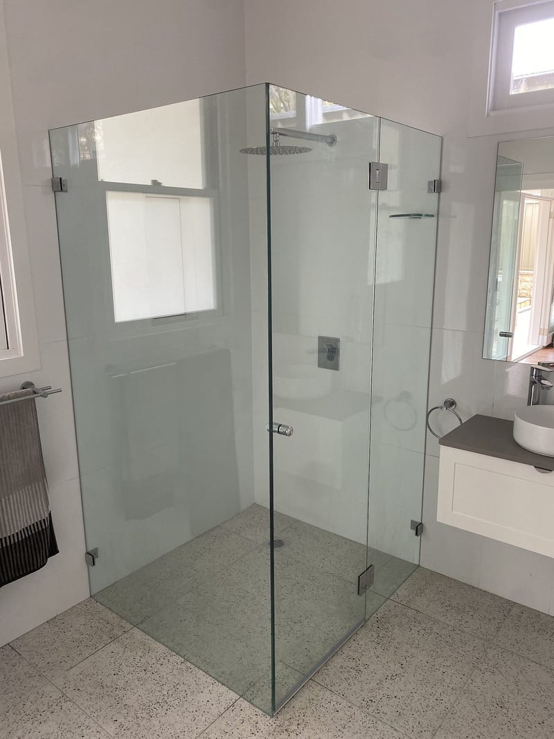 Frameless corner shower screen with hinge panel, door and return panel in polished chrome hardware on a terrazzo floor